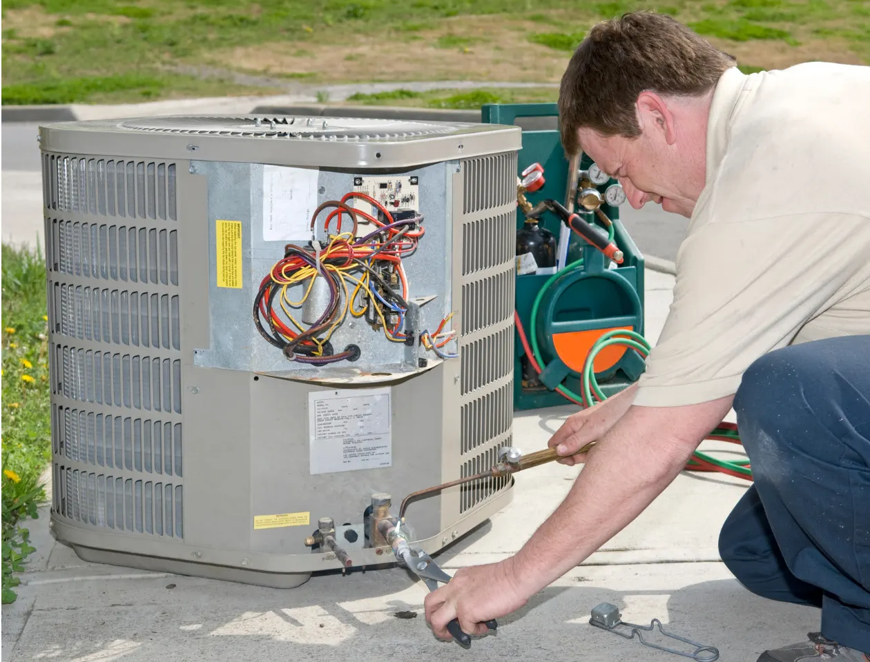 Person using HVAC tools to repair an outdoor air conditioning unit with wiring exposed and gauges nearby during maintenance work.